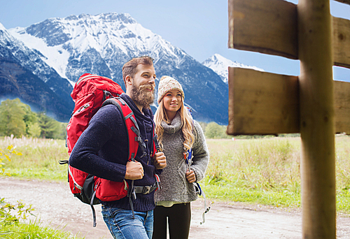 adventure, travel, tourism, hike and people concept - smiling couple with backpacks standing at signpost over mountains background