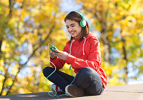 technology, season and people concept - smiling young woman or teenage girl with smartphone and headphones listening to music over autumn park background