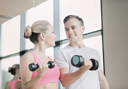 fitness, sport, exercising and diet concept - smiling young woman and personal trainer with dumbbells in gym