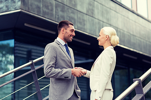 business, partnership, success, gesture and people concept - smiling businessman and businesswoman shaking hands on city street