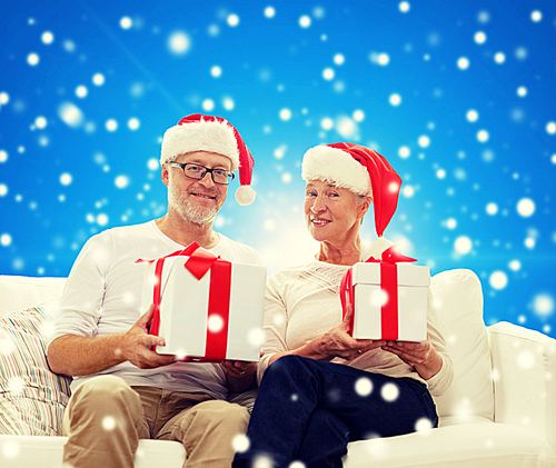 family, holidays, christmas, age and people concept - happy senior couple in santa helper hats with gift boxes over blue snowy background