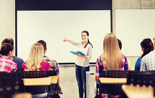 education, high school, teamwork and people concept - smiling student girl with notebook standing and pointing finger in front of students in classroom