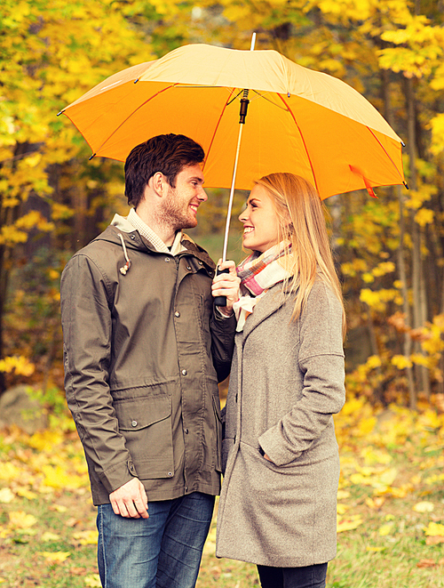 love, relationship, season, family and people concept - smiling couple with umbrella walking in autumn park