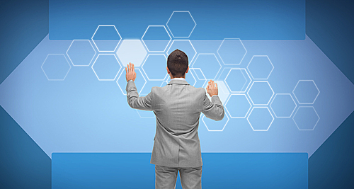 business, people, future technology, network and innovation concept - businessman in suit working with hexagonal projection on virtual screen over blue background from back