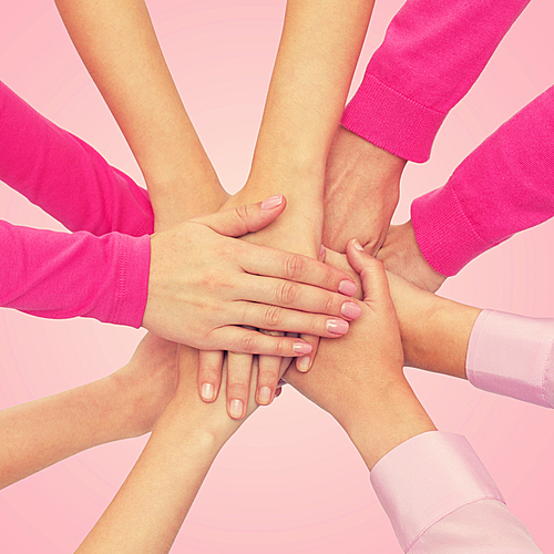 feminism, women power and breast cancer awareness concept - close up of women hands on top of each other over white background
