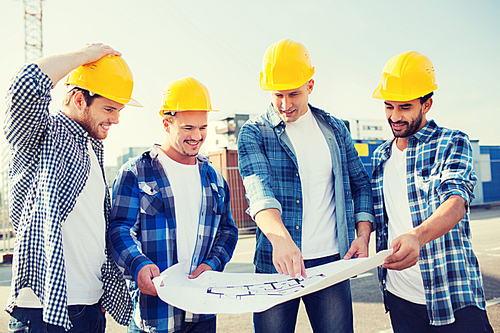 business, building, teamwork and people concept - group of smiling builders in hardhats with blueprint outdoors