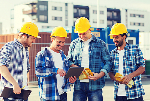 business, building, teamwork, technology and people concept - group of smiling builders in hardhats with tablet pc computer and clipboard outdoors