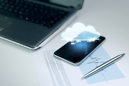 business, technology and information concept - close up of smartphone with cloud computing icon projection, laptop computer and chart with pen on office table