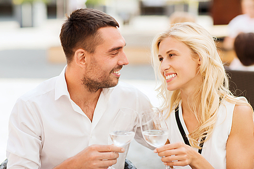 love, dating, people and holidays concept - smiling couple clinking glasses and looking to each other at restaurant lounge or terrace