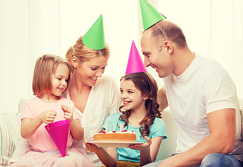 celebration, family, holidays and birthday concept - happy family with two kids in hats with cake at home