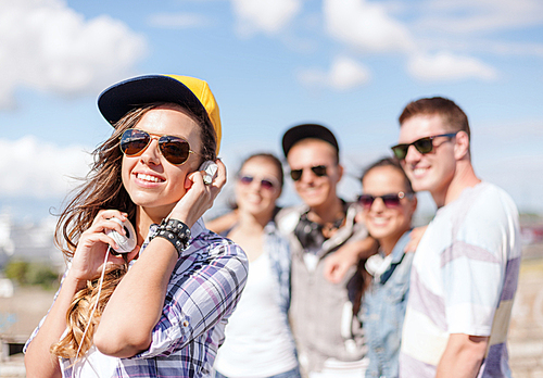 summer holidays and teenage concept - teenage girl in sunglasses, cap and headphones hanging out with friends outside