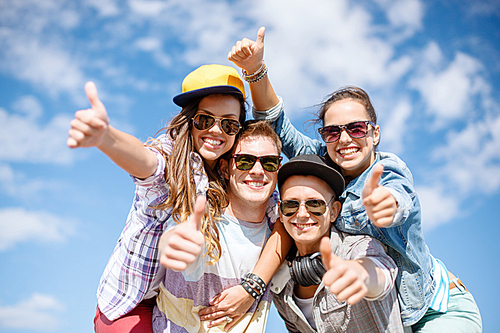 summer holidays and teenage concept - group of smiling teenagers in sunglasses hanging outside and showing thumbs up