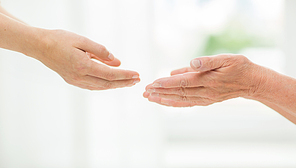 people, age, family, care and support concept - close up of senior woman and young woman reaching hands out to each other