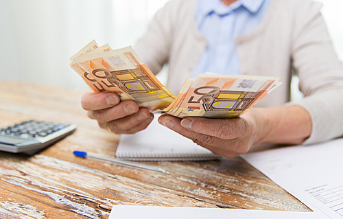 business, savings, annuity insurance, age and people concept - close up of senior woman with calculator and bills counting euro money at home