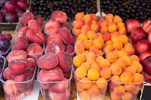 , harvest, food, fruits and agriculture concept - close up of flat peaches and apricots in plastic boxes at street market