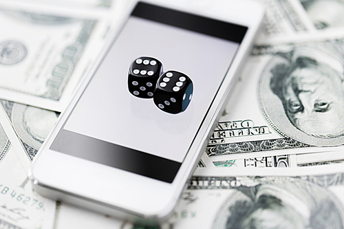 casino, online gambling, technology and fortune concept - close up of black dice, smart phone and dollar cash money