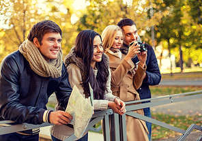 travel, vacation, technology, tourism and friendship concept - group of smiling friends with digital photo camera and map in city park