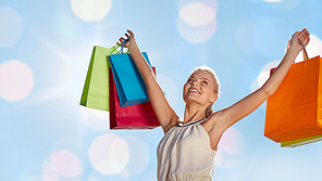 consumerism,  and people concept - smiling woman with shopping bag rising hands over blue lights background