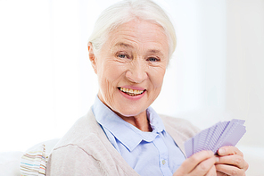 age, game, gamble, poker and people concept - happy smiling senior woman playing cards at home