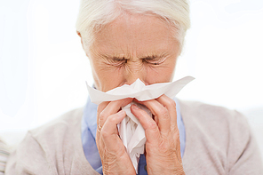 health care, flu, hygiene, age and people concept - sick senior woman blowing nose to paper napkin at home