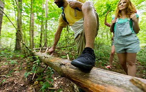 adventure, travel, tourism, hike and people concept - close up of friends hiking with backpacks and climbing over fallen tree trunk in woods