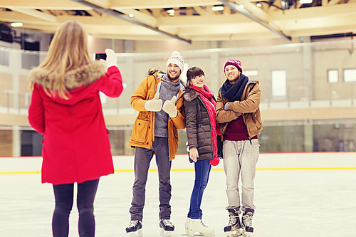 people, friendship, technology and leisure concept - happy friends taking photo with smartphone on skating rink