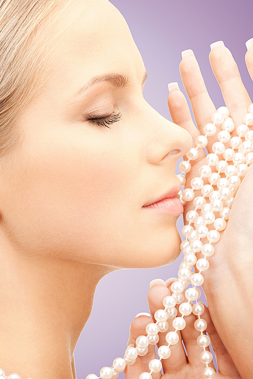 beauty, luxury, people, advertisement and jewelry concept - face of beautiful woman with sea pearls beads in hand over violet background