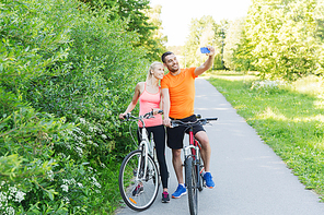 fitness, sport, people, technology and healthy lifestyle concept - happy couple with bicycle taking taking selfie by smartphone outdoors