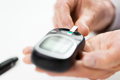 medicine, age, diabetes, health care and people concept - close up of senior woman with glucometer and test stripe checking blood sugar level at home