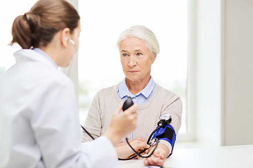 medicine, age, health care and people concept - doctor with tonometer checking senior woman blood pressure level at hospital