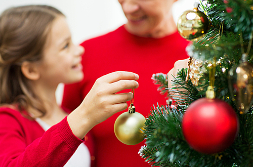 family, holidays, generation and people concept - close up of happy girl with grandmother decorating christmas tree at home