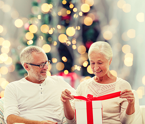 family, holidays, age and people concept - happy senior couple with gift box over christmas tree lights background