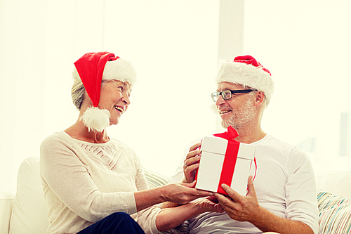 family, holidays, christmas, age and people concept - happy senior couple in santa helper hats with gift box at home