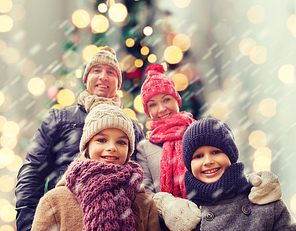 family, childhood, season, holidays and people concept - happy family in winter clothes over christmas tree lights background