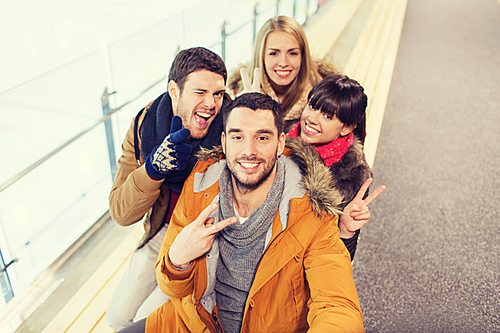 people, friendship, technology and leisure concept - happy friends taking selfie with camera or smartphone on skating rink