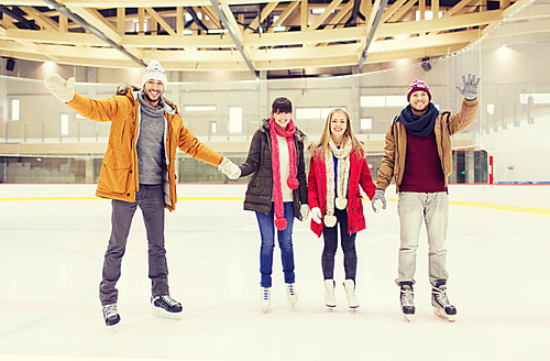 people, friendship, gesture, sport and leisure concept - happy friends waving hands on skating rink