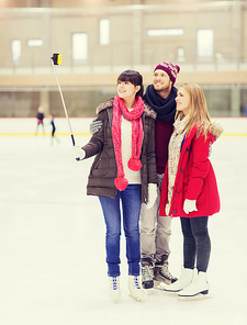 people, friendship, technology and leisure concept - happy friends taking picture with smartphone selfie stick on skating rink