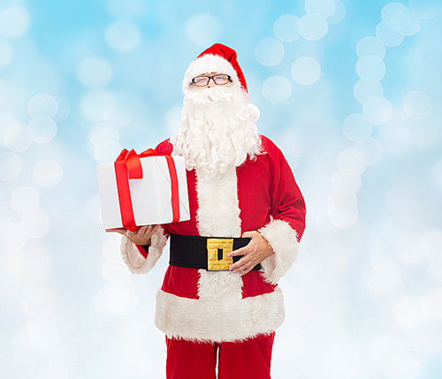 christmas, holidays and people concept - man in costume of santa claus with gift box over blue lights background