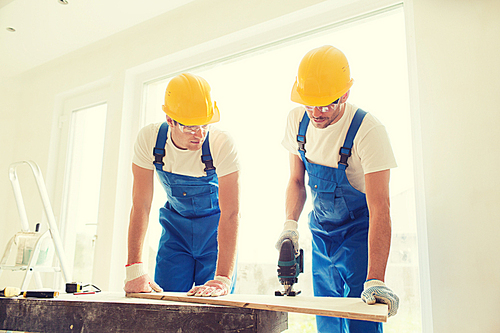 business, building, teamwork and people concept - group of smiling builders in hardhats with tools indoors