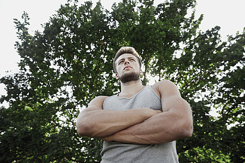 fitness, sport, people and healthy lifestyle concept - sporty young man with crossed arms at summer park