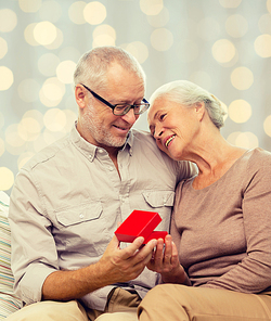 family, holidays, age and people concept - happy senior couple with little red gift box over lights background