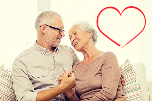 family, relations, love, age and people concept - happy senior couple hugging and holding hands on sofa at home with big red heart shape