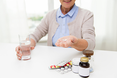 age, medicine, health care and people concept - close up of happy senior woman with pills and glass of water at home