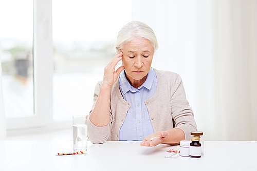 age, medicine, health care and people concept - senior woman with pills and glass of water at home