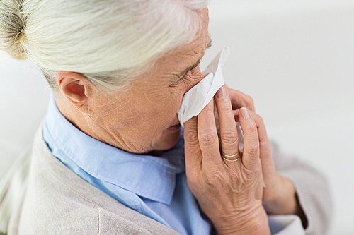health care, flu, hygiene, age and people concept - close up of sick senior woman blowing nose to paper napkin at home
