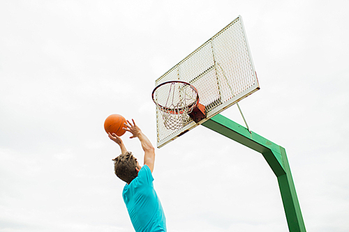 sport, game and basketball concept - young man throwing ball into basket outdoors