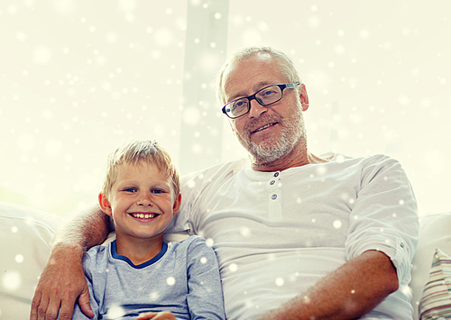 family, happiness, generation and people concept - smiling grandfather with grandson sitting on couch at home