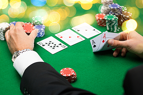 casino, gambling, poker, people and entertainment concept - close up of poker player with playing cards and chips at green casino table over holidays lights background