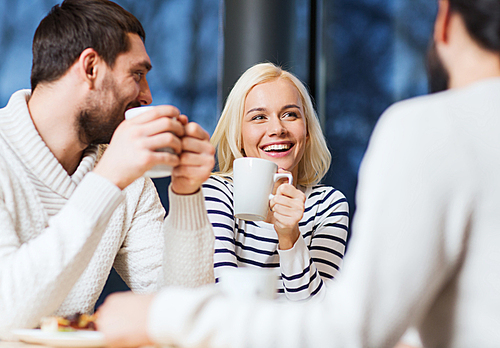 people, leisure, communication, eating and drinking concept - happy friends meeting and drinking tea or coffee at cafe