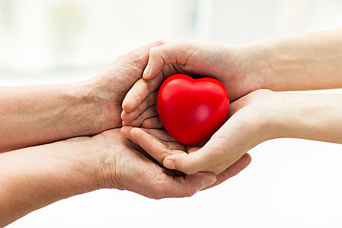 people, age, family, love and health care concept - close up of senior woman and young woman hands holding red heart